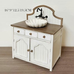 Pu&ograve; includere: Un mobiletto da toeletta in miniatura bianco e marrone con un lavandino smerlato e un rubinetto nero. Il mobile ha tre cassetti e due ante con pomelli in legno. Dimensioni: 40,6 cm x 22,9 cm x 31,8 cm/49,5 cm.