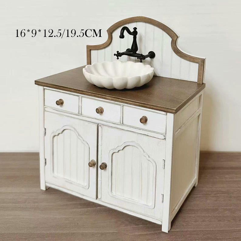 Pu&ograve; includere: Un mobiletto da toeletta in miniatura bianco e marrone con un lavandino smerlato e un rubinetto nero. Il mobile ha tre cassetti e due ante con pomelli in legno. Dimensioni: 40,6 cm x 22,9 cm x 31,8 cm/49,5 cm.