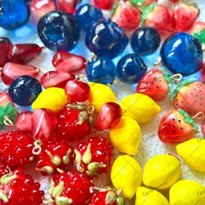 Puede incluir: Surtido de abalorios de colores con forma de fruta, incluyendo limones, fresas, frambuesas y arándanos. Los abalorios son de vidrio y tienen un acabado brillante.