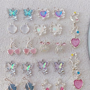 May include: Assortment of colorful charm pendants featuring butterflies, hearts, and other designs. The charms are made of metal and have a shiny finish.