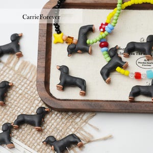 May include: A collection of small black dachshund figurines with gold accents. The figurines are arranged on a wooden tray with a colourful beaded necklace. The text "CarrieForever" is visible in the top left corner of the image.