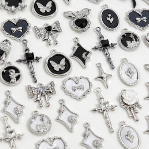 May include: Assortment of silver charm pendants with various designs, including butterflies, hearts, crosses, and stars. Some charms feature black and white enamel details.