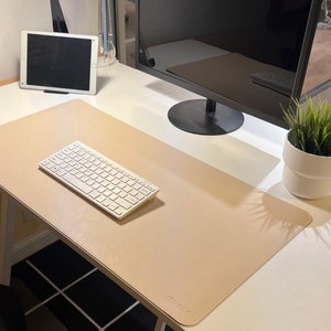 Schreibtischunterlage in der Farbe beige/braun. Die Größe ist 80 x 40 cm. Die Matte hat eine Korkunterlage. Sie ist ruschfest und wasserabweisend. Sie liegt auf einem Schreibtisch und eine Tastatur, Mauspad sowie ein Kaffe finden darauf Platz.