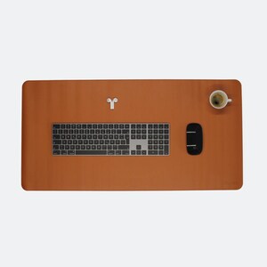 Ganze Matte ist zusehen in der Farbe cognac. Auf der Matte steht oben rechts ein Espresso. In der Mitte ist ein Magic Keyboard und mitte/rechts liegt eine Maustaste. Unten rechts steht das Logo NESK. Oben mittig liegen Airpods.