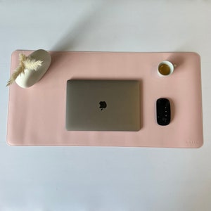 Ganze Matte ist zusehen in der Farbe rosé. Auf der Matte steht oben rechts ein Espresso. In der Mitte ist ein  Mac Book und mitte/rechts liegt eine Maustaste. Unten rechts steht das Logo NESK. Oben links steht eine Vase.