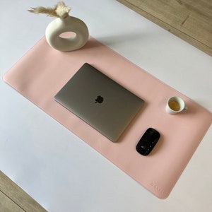 Ganze Matte ist zusehen in der Farbe rosé. Auf der Matte steht oben rechts ein Espresso. In der Mitte ist ein  Mac Book und mitte/rechts liegt eine Maustaste. Unten rechts steht das Logo NESK. Oben links steht eine Vase.