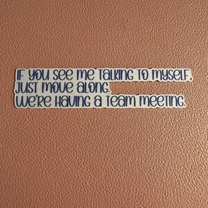 May include: A sticker with the text "IF YOU see mE TALKING TO MYSELF. JUST MOVE ALONG. We're Having a Team meeTING" in blue lettering on a brown background.