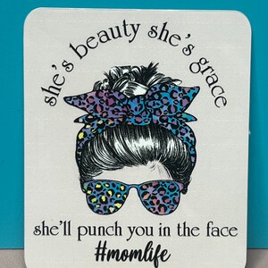 May include: A white background with a black and white illustration of a woman with a messy bun, wearing sunglasses and a leopard print headband. The text reads "she's beauty she's grace she'll punch you in the face #momlife"