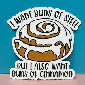 Peut inclure: Un autocollant blanc avec une illustration de pain à la cannelle et le texte "Je veux des buns d'acier mais je veux aussi des buns à la cannelle".