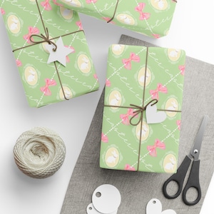 May include: Wrapped gifts with green Easter-themed paper featuring white rabbits, pink bows, and the word "Easter". Each package is tied with twine and a white paper tag. A ball of twine, scissors, and blank tags are also visible.