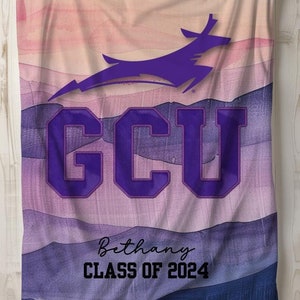 以下が含まれることがあります： 紫と青の水彩画風の毛布で、山脈のデザインが施されています。毛布には、「GCU」という文字が大きく太字で書かれており、紫色の山ライオンのシルエットが描かれています。「Bethany CLASS OF 2024」という文字も毛布に書かれています。