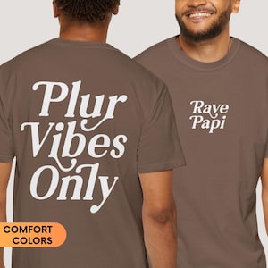 May include: A brown t-shirt with the text "Plur Vibes Only" on the back and "Rave Papi" on the front. The shirt is made of a soft, comfortable fabric.