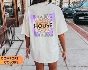 May include: A cream colored t-shirt with a graphic of the word "HOUSE" repeated five times in a stacked pattern. The word "HOUSE" is in black text with a purple outline and a yellow butterfly graphic behind each word.
