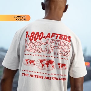 Op de afbeelding: Wit T-shirt met een rode grafische print van de tekst "1-800-AFTERS", drie keer herhaald. De grafiek bevat ook een wereldkaart en de tekst "THE AFTERS ARE CALLING".