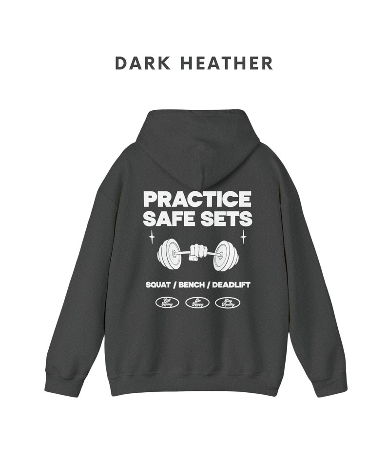 K&ouml;nnte beinhalten: Dunkelgrauer Kapuzenpullover mit einem wei&szlig;en Grafikdruck, der "Practice Safe Sets" mit einer Langhantel und den Worten "Squat / Bench / Deadlift" darunter sagt. Die Grafik enth&auml;lt auch drei kleine Kreise mit den Worten "Safe Heavy" darin.