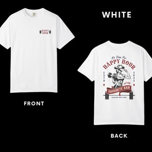 Op de afbeelding: Wit T-shirt met een ontwerp van "HAPPY HOUR" en een halter op de voorkant. De achterkant heeft een afbeelding van een gewichtheffer met de tekst "It's Time For HAPPY HOUR at my FAVORITE BAR GAINS ON TAP 2023".