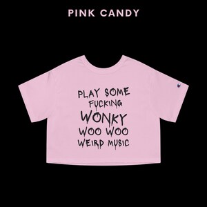 K&ouml;nnte beinhalten: Hellrosa Crop-Top mit dem schwarzen Text "PLAY SOME FUCKING WONKY WOO WOO WEIRD MUSIC". Dar&uuml;ber steht "PINK CANDY". Das Shirt hat kurze &Auml;rmel. Das Champion-Logo ist sichtbar.