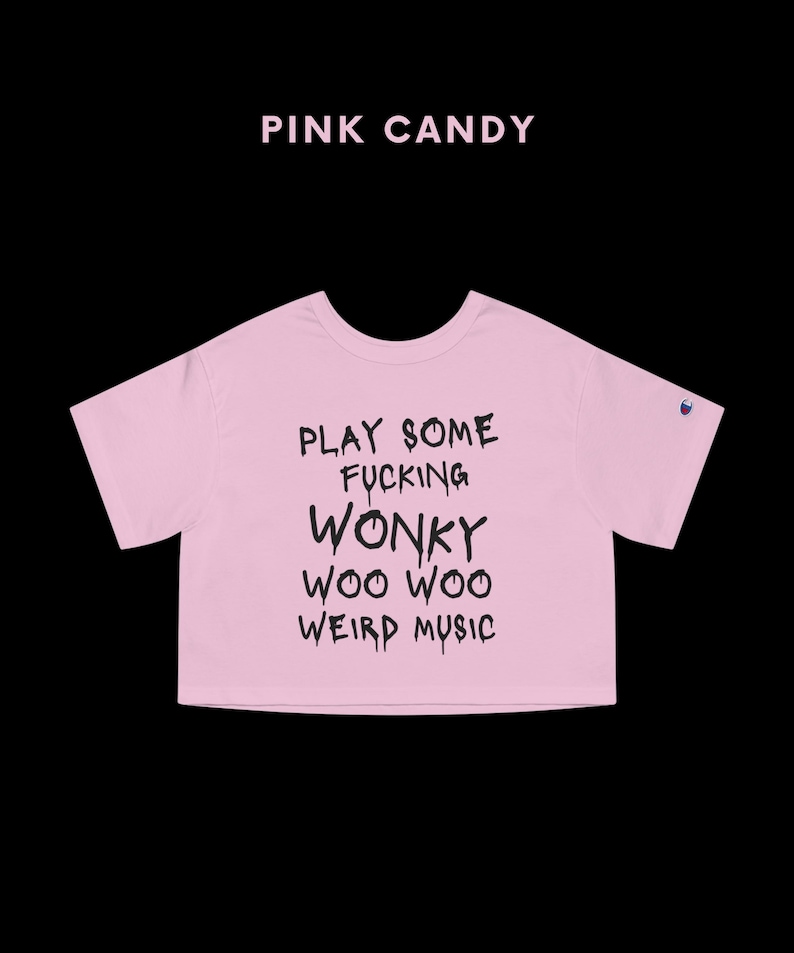 K&ouml;nnte beinhalten: Hellrosa Crop-Top mit dem schwarzen Text "PLAY SOME FUCKING WONKY WOO WOO WEIRD MUSIC". Dar&uuml;ber steht "PINK CANDY". Das Shirt hat kurze &Auml;rmel. Das Champion-Logo ist sichtbar.