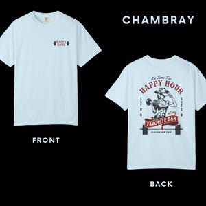 Op de afbeelding: Lichtblauw t-shirt met "HAPPY HOUR" op de voorkant. De achterkant toont een afbeelding van een gewichtheffer met de tekst "It's Time For HAPPY HOUR at my FAVORITE BAR GAINS ON TAP 2023".
