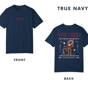 May include: A navy blue t-shirt with the text "YOU DIED" printed on the front in red. The back of the shirt features a graphic of a knight sitting on a throne with swords and the text "YOU DIED" printed in red.