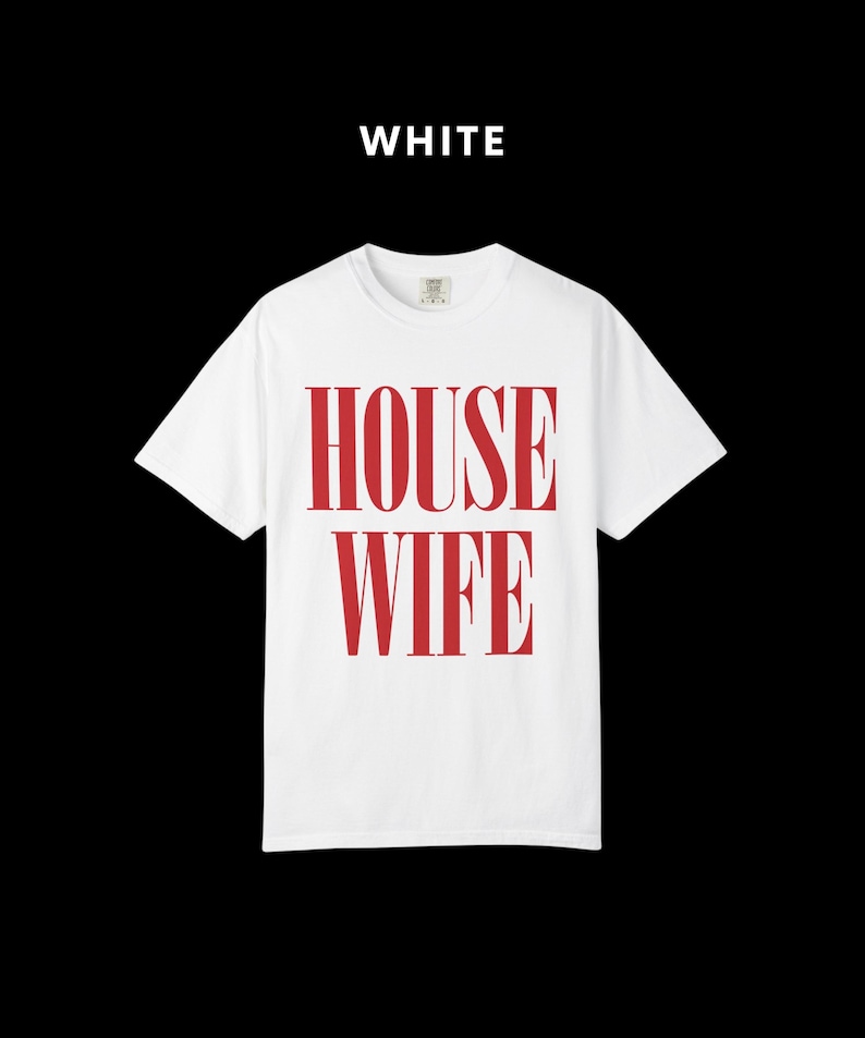 May include: White t-shirt with the word "HOUSEWIFE" printed in red. The text is vertically aligned and centered on the shirt. The word "WHITE" is printed above the shirt. The shirt has short sleeves and a crew neck.