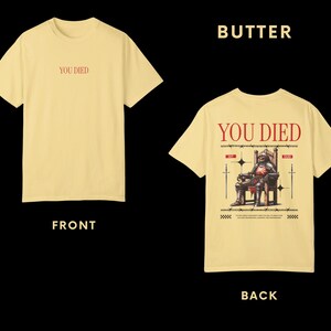 May include: A yellow t-shirt with the text "YOU DIED" on the front and a graphic of a knight sitting on a throne with the same text on the back.