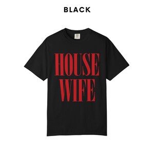 May include: Black t-shirt with the word "HOUSEWIFE" in large, red, bold letters. The word "BLACK" is printed above the shirt. The shirt is a classic crew neck style.