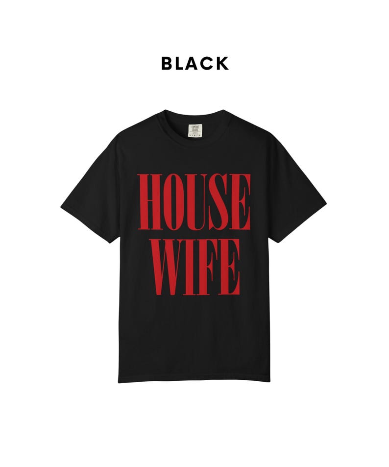 May include: Black t-shirt with the word "HOUSEWIFE" in large, red, bold letters. The word "BLACK" is printed above the shirt. The shirt is a classic crew neck style.