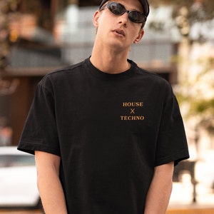 Pu&ograve; includere: Una persona indossa una maglietta nera con la scritta "HOUSE x TECHNO" stampata sul davanti. La persona indossa un berretto nero e occhiali da sole.