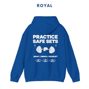 K&ouml;nnte beinhalten: Royalblauer Kapuzenpullover mit wei&szlig;em Text, der "Practice Safe Sets" lautet, und einer Grafik einer Person, die eine Langhantel hebt. Der Text "Squat / Bench / Deadlift" befindet sich unter der Grafik. Drei kleine wei&szlig;e Kreise mit dem Text "Safe Lifting" befinden sich unter dem Text.