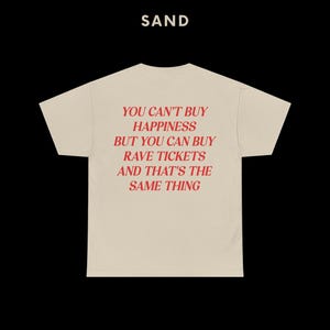 May include: A beige t-shirt with the text "YOU CAN'T BUY HAPPINESS BUT YOU CAN BUY RAVE TICKETS AND THAT'S THE SAME THING" printed in red.