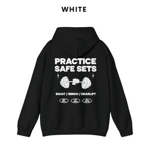 K&ouml;nnte beinhalten: Schwarzer Kapuzenpullover mit dem Text "PRACTICE SAFE SETS" und einer Grafik einer Langhantel, die von einer Hand gehalten wird. Der Text "SQUAT / BENCH / DEADLIFT" befindet sich unter der Grafik. Drei kleine Kreise mit dem Text "Safe Heavy" befinden sich unter dem Text.