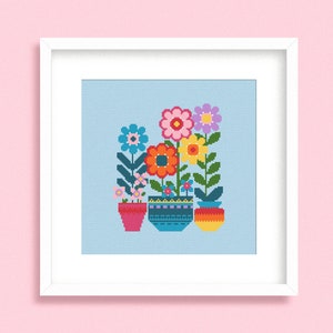 May include: A framed cross-stitch artwork depicting vibrant flowers in patterned pots. The flowers are in shades of pink, orange, yellow, and purple, with green foliage. The pots are red, teal, and yellow. The background is a light blue colour.