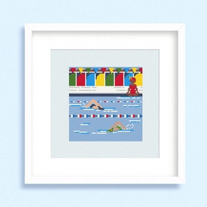 May include: Cross-stitch artwork of a swimming competition. The image features swimmers in a blue pool with lane markers. Above the pool are colorful flags and a lifeguard in a red outfit. The artwork is framed in a white square frame.