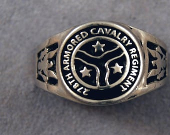 Puede incluir: Un anillo de plata con un diseño de esmalte negro. El anillo tiene el texto "81st Armored Cavalry Regiment" y tres estrellas.