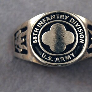 Op de afbeelding: Een zilveren ring met een zwarte emailleband met de inscriptie "88th Infantry Division U.S. Army". De ring heeft een zilveren vierpuntige stervorm in het midden.