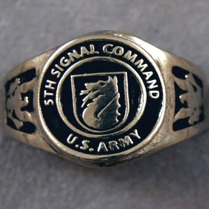 May include: A silver ring with a black enamel design. The ring features the words "5th Signal Command" and "U.S. Army" around a crest with a wolf's head.