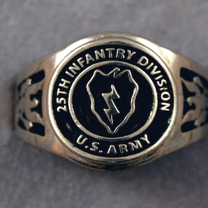May include: A silver ring with a black enamel inlay featuring the 25th Infantry Division insignia. The ring has a U.S. Army inscription.
