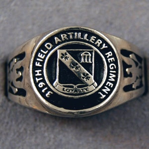 May include: A silver ring with a black enamel crest featuring the text "19th Field Artillery Regiment" and the words "Loyalty" on a banner. The crest also includes a shield with three fleurs-de-lis and a building.