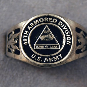 May include: A silver ring with a black enamel design. The ring features the words "49th Armored Division" and "U.S. Army" around a black triangle with the number "49" and the words "Lone Star" inside.