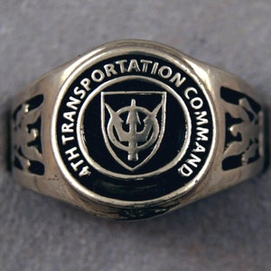 May include: A silver ring with a black enamel design. The design features a shield with a trident and the words "4TH TRANSPORTATION COMMAND".
