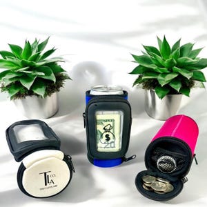 May include: Three different colored can coolers with a zippered pocket and a clear window for cash or cards. The coolers are black, blue, and pink. The text on the white cooler says "T.L.A. Co. They Love Are."