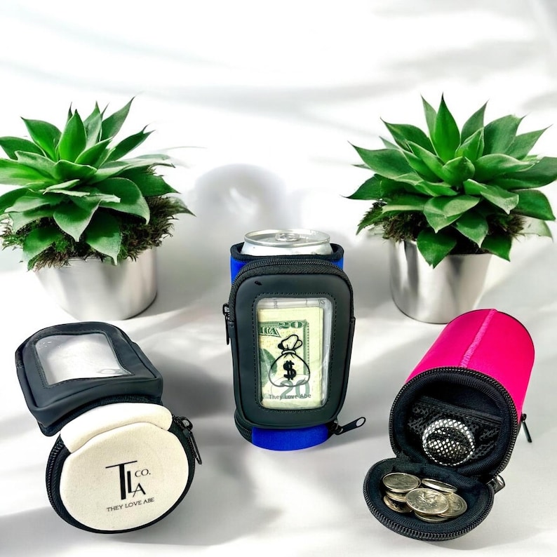 May include: Three different colored can coolers with a zippered pocket and a clear window for cash or cards. The coolers are black, blue, and pink. The text on the white cooler says "T.L.A. Co. They Love Are."