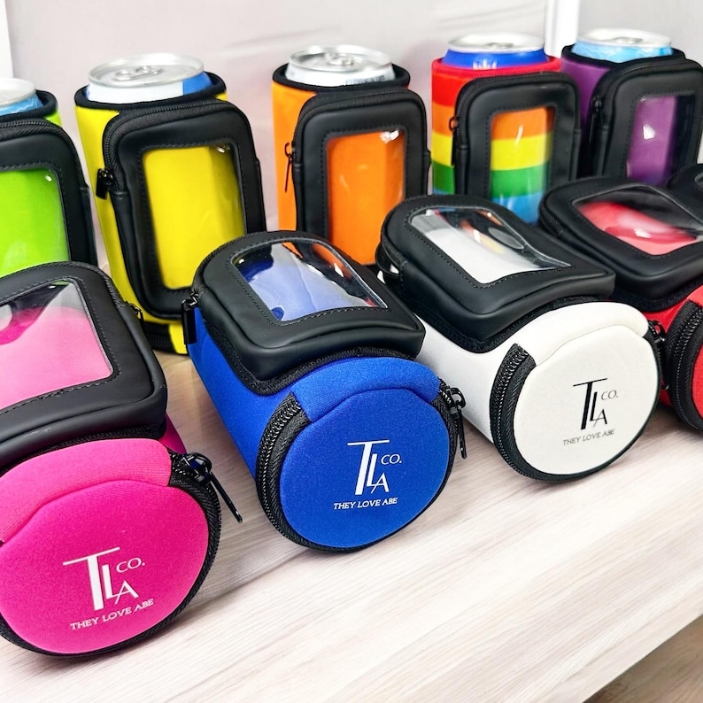 May include: Assortment of colorful neoprene can coolers with a clear window and a zipper closure. Each cooler features a circular logo with the text "T.co. LA THEY LOVE ABE".