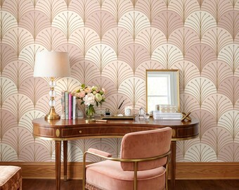 May include: A curved wooden desk with a gold-trimmed edge, a lamp with a clear glass base, a bouquet of flowers, and a stack of books. A pink velvet chair with a gold frame sits in front of the desk against a wallpaper with a fan-shaped pattern.