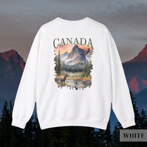 May include: White sweatshirt with a graphic print of a mountain landscape with a deer and an eagle. The text "CANADA" is printed above the graphic.
