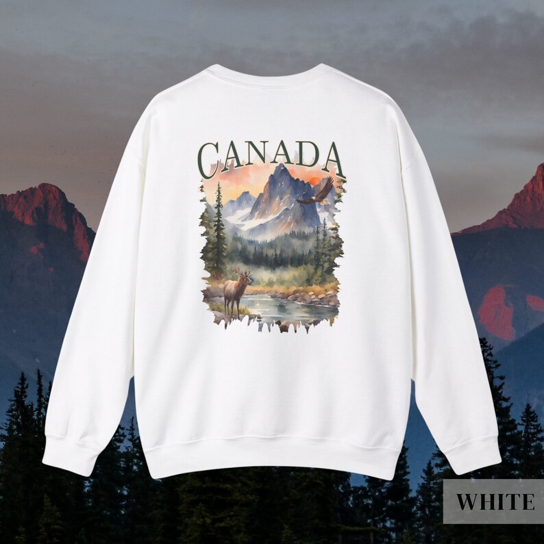 May include: White sweatshirt with a graphic print of a mountain landscape with a deer and an eagle. The text "CANADA" is printed above the graphic.