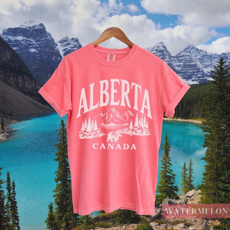 May include: A pink t-shirt with a white graphic design featuring a mountain range, a bear, and the text "ALBERTA CANADA".