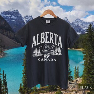 May include: Black t-shirt with a white graphic design featuring a mountain range, a bear, and the text "ALBERTA CANADA".