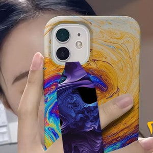 May include: A phone case with a colorful abstract design and a purple phone grip. The case has a white background with swirls of yellow, blue, green, and red.